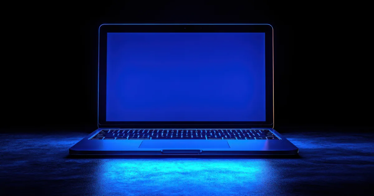 A laptop glowing with a blank blue screen in a dark room, like an app that will not load.